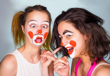 Alay, kavramı alay. Parmaklarını birbirlerine dönük ve gülümseyen iki arkadaş. Atış, arka planı gri studio. Aile renk arka plan üzerinde komik kılık. April fools'day kutlama