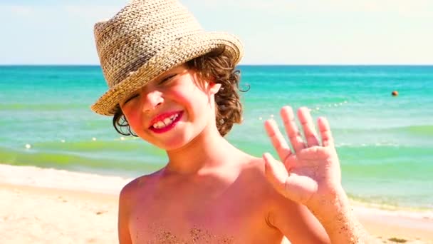 青空をバックにビーチで麦わら帽子立っているの巻き毛を持つ少年 — ストック動画