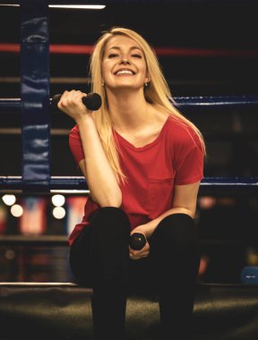 Güzel seksi kadın bir boks yüzüğü kenarında Dambıl ile oturan spor giyim giyiyor. Boxer kız kadınlık ve acımasız spor konsepti pozitif.