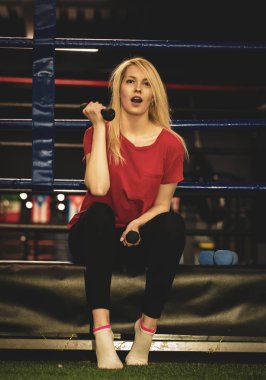 Güzel seksi kadın bir boks yüzüğü kenarında Dambıl ile oturan spor giyim giyiyor. Boxer kız kadınlık ve acımasız spor konsepti pozitif.