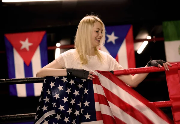 Success woman celebrating for her succes with the flag of USA. Female boxer with the USA flag is in training near the ring. Patriot and fan concept.