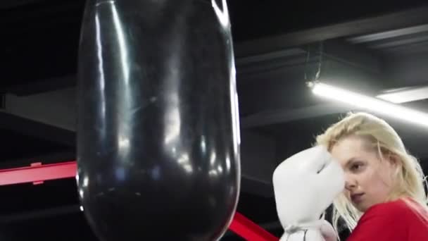 美丽的金发女子拳击手训练与打孔袋在健身房 — 图库视频影像