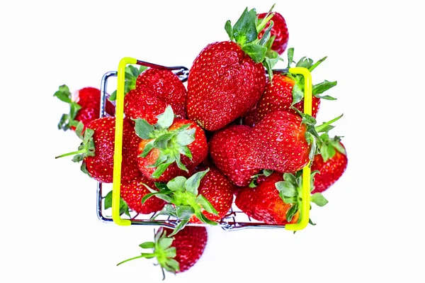 Self-service supermarket shopping basket with fresh strawberries, grocery products on a light background. View from above