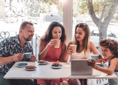 Kahvaltı ve tablet kullanarak mutlu bir aile. Mutlu bir adam ve internet, kullanarak seyir perde için üç çocukları gülümseyen kafe, dijital tablet olan büyük bir şirket online satın
