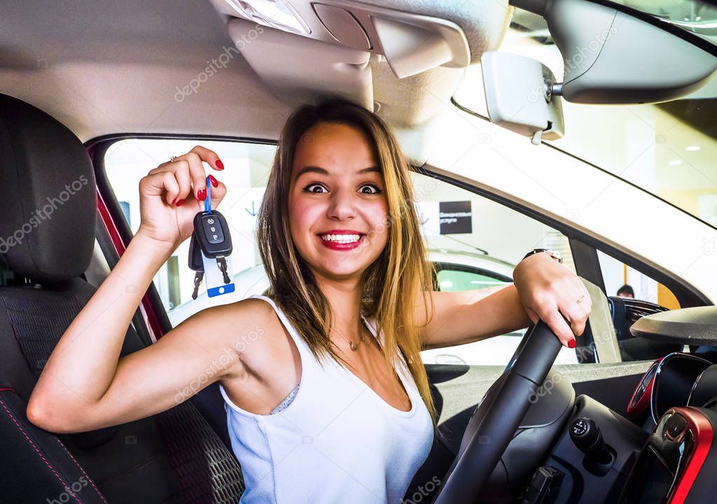 Young pretty woman happy and smiling, holding the keys of the white car, confident, offering them to start your new car