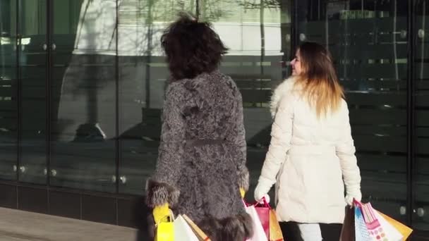 两个女孩穿着冬装在户外散步 手里拿着购物袋 现代城市背景 慢动作 — 图库视频影像