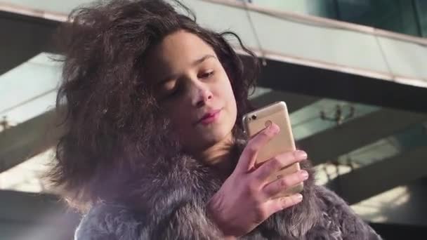 年轻的卷发女孩在冬天的衣服使用智能手机 商场背景 慢动作 — 图库视频影像