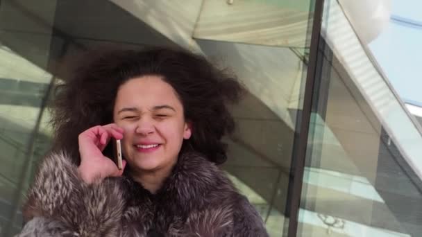 Jonge Krullend Meisje Winterkleren Praten Smartphone Overdag Moderne Stad Achtergrond — Stockvideo