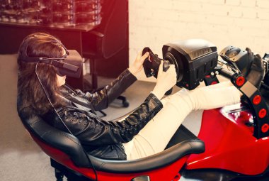 Kız başında vr kulaklık ile bir arabanın simülatöroturur ve oyun oynar. Kadın sanal gerçeklik odası oyun kulübünde yarış oynar.