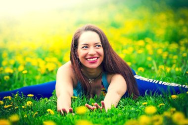 Kız germe egzersizleri pratik. Güzel genç kadın parkta yeşil çim üzerinde egzersiz germe yapıyor. Pozitif duygular kavramı.