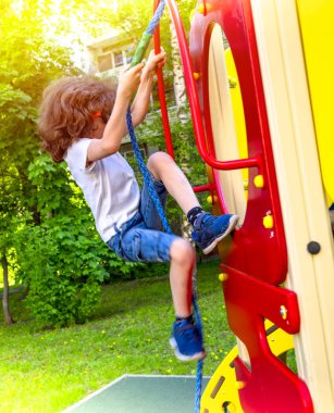 Küçük kıvırcık çocuk oyun alanında oynuyor. Eğlenceli ve açık oyun üzerinde tırmanma mutlu Shaggy çocuk çocuk. İp kullanarak komik neşeli çocuk. Aktif çocuk için yaz, İlkbahar ve sonbahar eğlence.