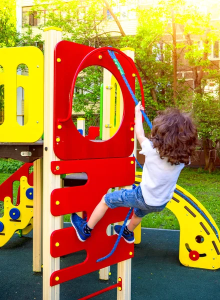 小さなカーリー少年が遊び場で遊んでいます 楽しさと屋外の遊び場に登っている幸せなシャギーの子供の男の子 ロープを使って面白い喜びの子供 アクティブな子供のための夏 秋のレジャー — ストック写真