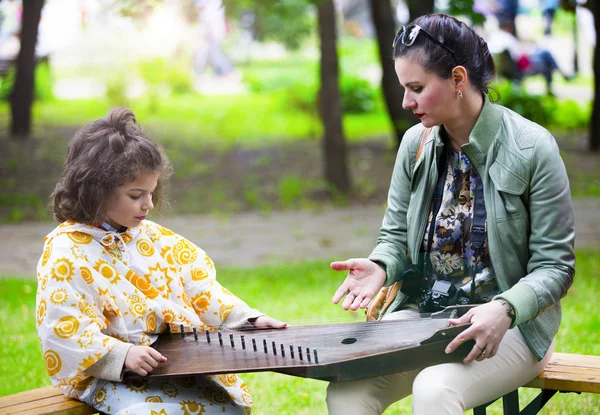 Mom teaches to play a little son on a harp in a picturesque park. Maintaining traditions concept