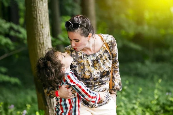 Mom is hugging and kissing her son. Woman hugging a little boy outdoor. The concept of family in nature, gentle embrace. The landscape and forest. Tenderness and maternal love concept