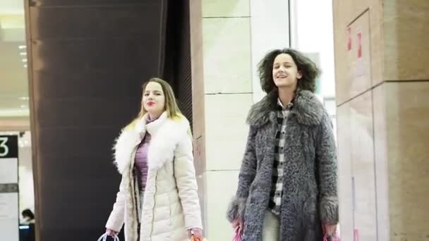 冬服を着た2人の女の子が買い物袋を手にしてモールを歩いている スローモーション — ストック動画