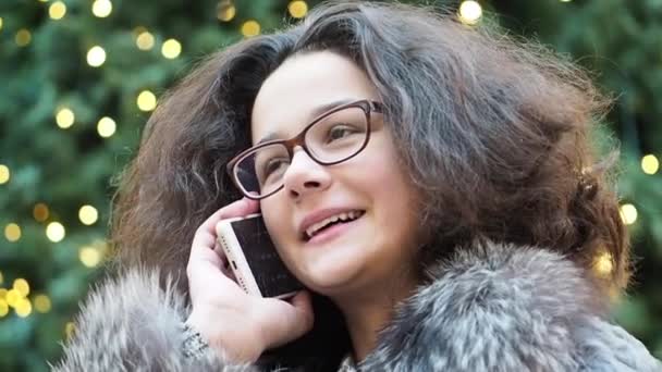 Jonge Krullend Meisje Brillen Praten Smartphone Wazig Kerstboom Achtergrond Slow — Stockvideo