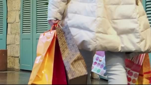 冬服を着た2人の女の子が買い物袋を手にしてモールを歩いている スローモーション — ストック動画