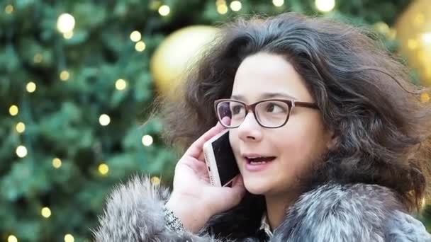 Młoda Dziewczyna Kręcone Okularach Mówić Smartfonie Niewyraźne Tło Choinki Zwolnionym — Wideo stockowe