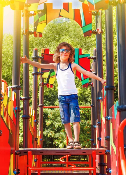 その少年は通りの遊び場で楽しんでいる 子供のための公園でのスイングやスライド 子供の遊び場は明るくカラフルです 市内の公園の子供のための近代的な子供の遊び場 — ストック写真