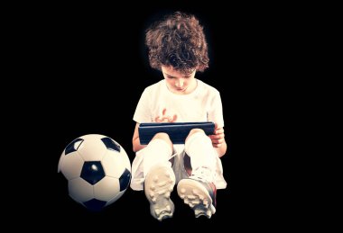 Siyah duvar arka plan üzerinde tablet duvar bilgisayarı kullanarak, futbol topu ile şaşkın küçük çocuk futbol oyuncusu. İnsanlar duygular, spor aile eğlence yaşam tarzı kavramı