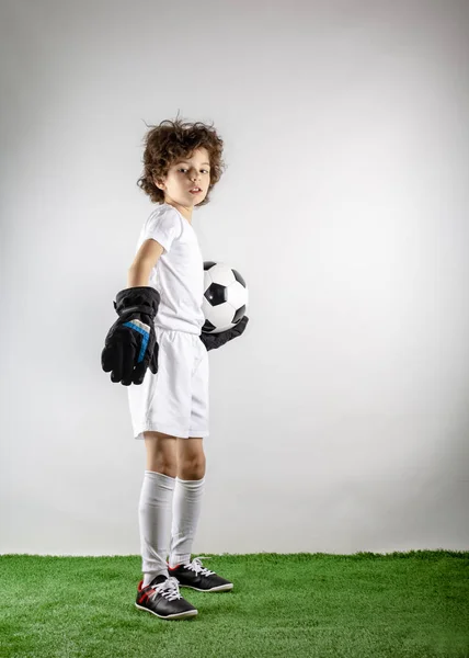 Kid - soccer champion. Boy goalkeeper in football sportswear with ball on gray background. Sport concept. Copy space.