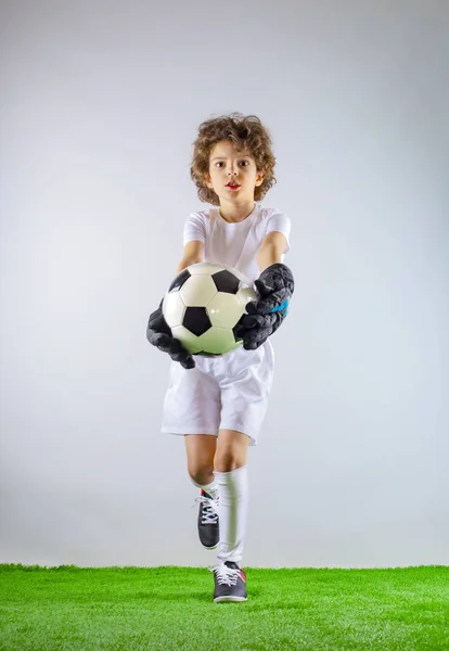 Kid - soccer champion. Boy goalkeeper in football sportswear with ball on gray background. Sport concept. Copy space.