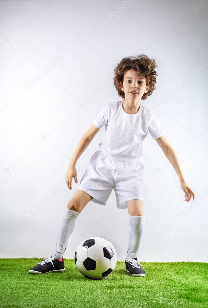 Boy with soccer ball on the green grass. Excited little toddler boy playing football on soccer field against light background. Active childhood and sports passion concept. Save space