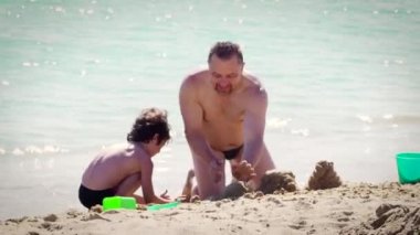 Baba ve oğul kumlu sahilde gündüz eğleniyorlar. 