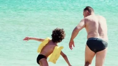 Baba ve oğul kumlu sahilde gündüz eğleniyorlar. 