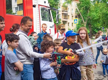 Moskova, Rusya - 07 Ağustos 2019: İtfaiyeci gibi davranan ve su sıçratan mutlu çocuklar. Elinde hortum la bir okul grubunda çocuk ve yetişkin itfaiyeci oynarken.