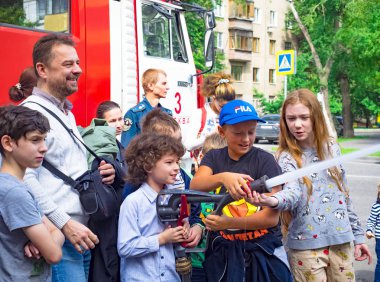 Moskova, Rusya - 07 Ağustos 2019: İtfaiyeci gibi davranan ve su sıçratan mutlu çocuklar. Elinde hortum la bir okul grubunda çocuk ve yetişkin itfaiyeci oynarken.