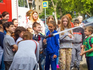 Moskova, Rusya - 07 Ağustos 2019: İtfaiye. İtfaiyeci gibi davranan ve elinde ateş hortumu olan ve su sıçratan mutlu çocuklar. Elinde hortumlu çocuk itfaiyeciyi oynuyor.