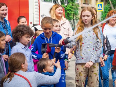 Moskova, Rusya - 07 Ağustos 2019: İtfaiye. İtfaiyeci gibi davranan ve elinde ateş hortumu olan ve su sıçratan mutlu çocuklar. Elinde hortumlu çocuk itfaiyeciyi oynuyor.