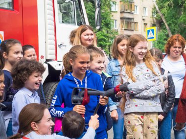 Moskova, Rusya - 07 Ağustos 2019: İtfaiye. İtfaiyeci gibi davranan ve elinde ateş hortumu olan ve su sıçratan mutlu çocuklar. Elinde hortumlu çocuk itfaiyeciyi oynuyor.