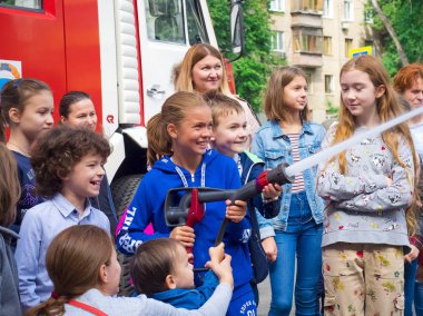 Moskova, Rusya - 07 Ağustos 2019: İtfaiye istasyonunda yangın hortumu deneyen ve su püskürten, bir itfaiyecinin yardım ettiği çocukların ve ebeveynlerin yan görünümü