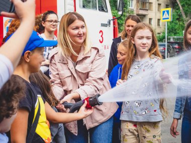 Moskova, Rusya - 07 Ağustos 2019: İtfaiye. İtfaiyeci gibi davranan ve elinde ateş hortumu olan ve su sıçratan mutlu çocuklar. Elinde hortumlu çocuk itfaiyeciyi oynuyor.