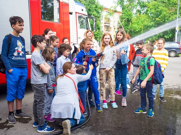 Moskova, Rusya - 07 Ağustos 2019: İtfaiye. İtfaiyeci gibi davranan ve elinde ateş hortumu olan ve su sıçratan mutlu çocuklar. Elinde hortumlu çocuk itfaiyeciyi oynuyor.
