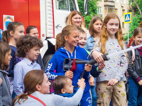 Moskova, Rusya - 07 Ağustos 2019: İtfaiye. İtfaiyeci gibi davranan ve elinde ateş hortumu olan ve su sıçratan mutlu çocuklar. Elinde hortumlu çocuk itfaiyeciyi oynuyor.