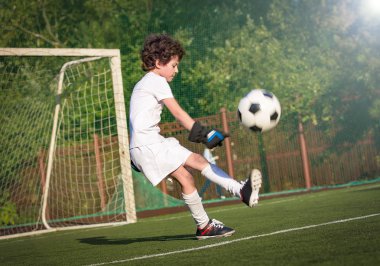 Futbol sahasında koşan beyaz giysili bir çocuk. Genç futbolcu futbolda top sürüyor ve topa vuruyor. Eğitim, aktif yaşam tarzı, spor, çocuk aktivitesi konsepti. seçici odak