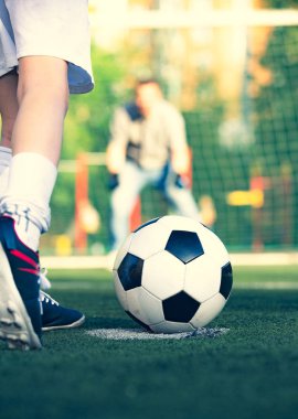 Babasıyla futbol sahasında oynayan küçük bir çocuk. Çocuk futbolcu bir futbol sahasına atış yapmaya hazırlanıyor.