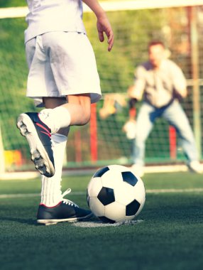 Babasıyla futbol sahasında oynayan küçük bir çocuk. Çocuk futbolcu bir futbol sahasına atış yapmaya hazırlanıyor.