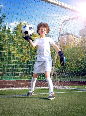 Babasıyla futbol sahasında oynayan küçük bir çocuk. Çocuk futbolcu sahada atış yapmaya hazırlanıyor. Futbol sahasında genç bir kaleci futbol kapısında duruyor..