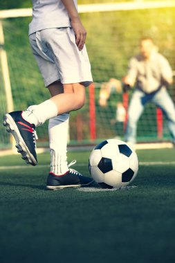 Babasıyla futbol sahasında oynayan küçük bir çocuk. Çocuk futbolcu bir futbol sahasına atış yapmaya hazırlanıyor.