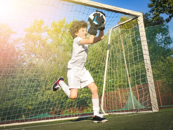 Soccer goalkeeper child in action.Goalkeeper catching the ball. Football soccer game. Boys on the sports field at daytime. Training and practicing.