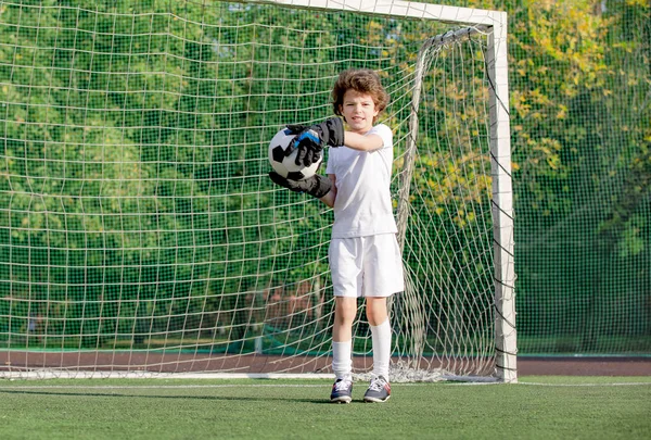 Boy in white sportswear running on soccer field. Young footballer dribble and kick football ball in game. Training, active lifestyle, sport, child activity concept. selective focus