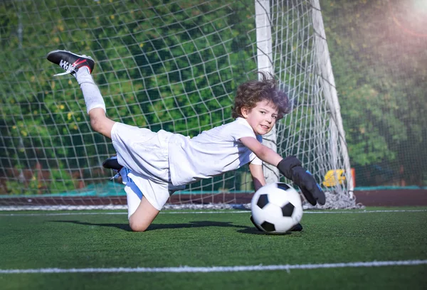 Young soccer goalie attempting to make a save. Little soccer goalkeeper with gloves. Kid - soccer champion. Boy goalkeeper in football sportswear on stadium with ball. Sport concept.