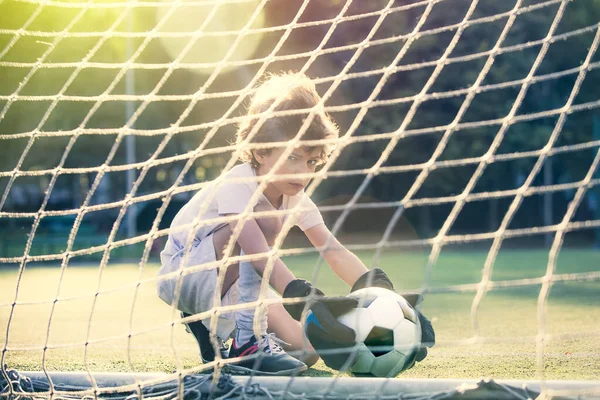 Disappointed football team goalkeeper following goals. Soccer Ball in the grid of gate, the team player pulls the scored the ball out of the goal on green field. Defeat Concept