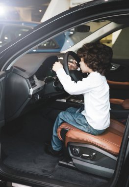 Satıcılıkta çocuk gözlemleme ve yeni arabayı test etme. Küçük çocuk sürücü koltuğunda oturuyor, araba kulübesinde. Küçük çocuk direksiyonda el ele tutuşuyor, gülümsüyor..