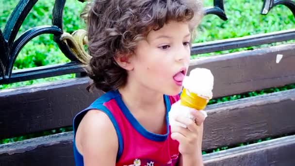 小さな子供がベンチでアイスクリームを食べている映像です — ストック動画