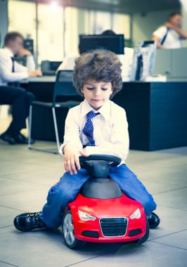 Kravat takan ve gömlek giyen sevimli, komik bir çocuk küçük kırmızı bir oyuncak arabanın üzerinde oturuyor. Kıvırcık saçlı esmer çocuk oto kuaförde eğleniyor. İş galerisi kavramı